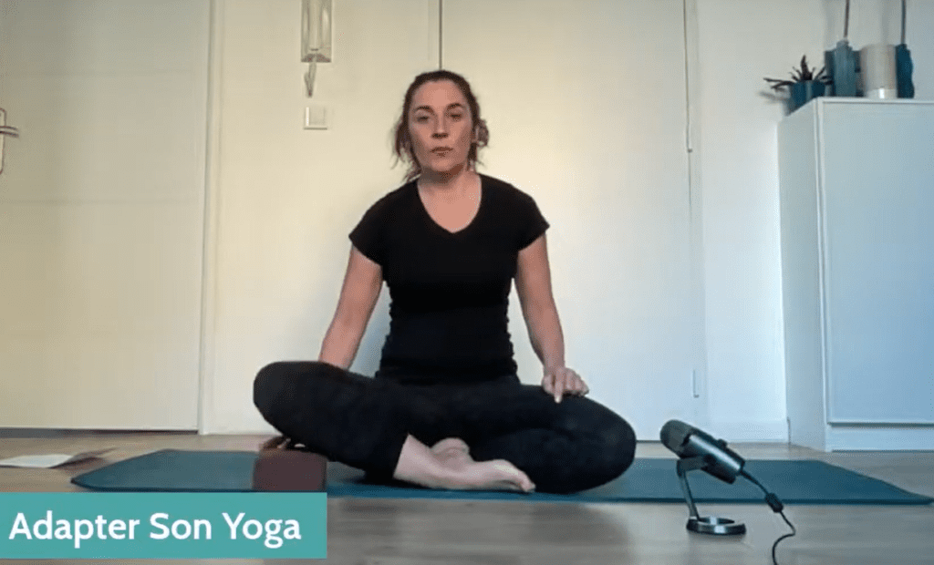 Femme en position assise sur son tapis de yoga avec une brique sous le genou pour pratiquer la respiration abdominale pour la colopathie fonctionnelle.